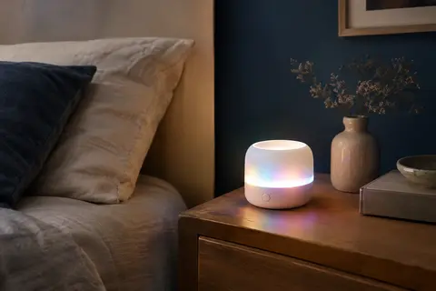 Machine à bruit blanc blanche avec veilleuse lumineuse posée sur une table de chevet en bois