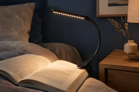 Lampe de lecture noire à pince et col flexible fixée à un livre dans une chambre tamisée.