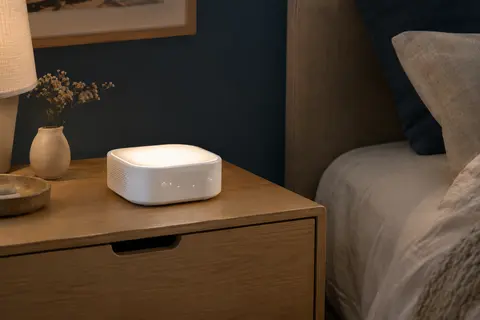 Machine à bruit blanc blanche posée sur une table de chevet en bois dans une chambre tamisée