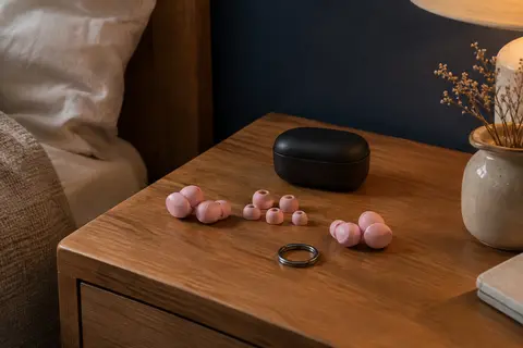 Deux paires de bouchons d’oreilles roses avec embouts interchangeables et étui noir sur une table de chevet.