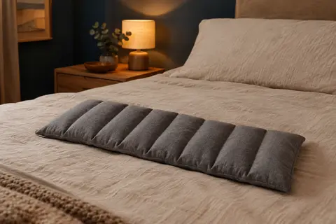 Coussin chauffant Leschi gris en coton, posé sur un lit en lin dans une chambre à la lumière douce