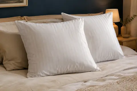 Deux oreillers carrés blancs à fines rayures satinées posés sur un lit dans une chambre calme