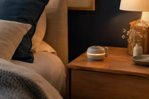 Générateur de bruit blanc portable avec clip et veilleuse ambrée posé sur une table de chevet