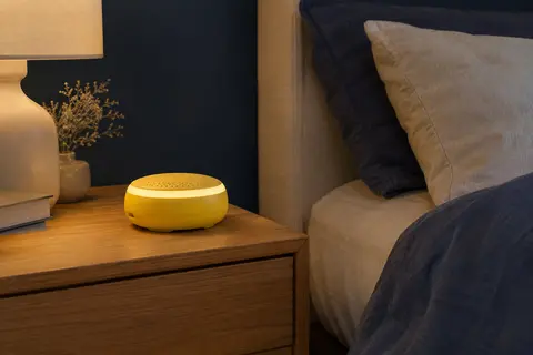 Machine à bruit blanc Momcozy jaune avec veilleuse tactile posée sur une table de chevet en bois