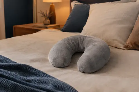 Bouillotte sèche grise en forme de tour de cou posée sur un lit dans une chambre aux tons doux.