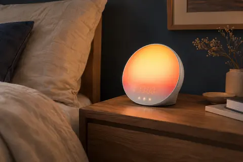 Éveil lumière Philips blanc posé sur une table de nuit en bois dans une chambre calme