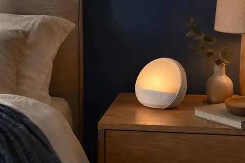 Réveil simulateur d’aube blanc posé sur une table de chevet en bois dans une chambre tamisée